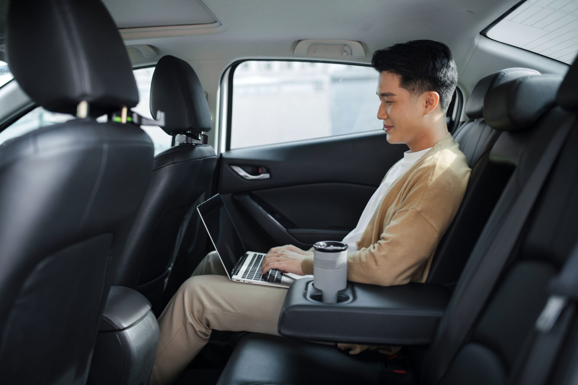 Man working on a laptop sitting in the backseat of a car