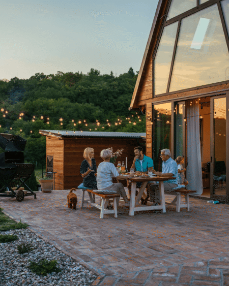 A-frame house at dusk with people gathered on the patio below