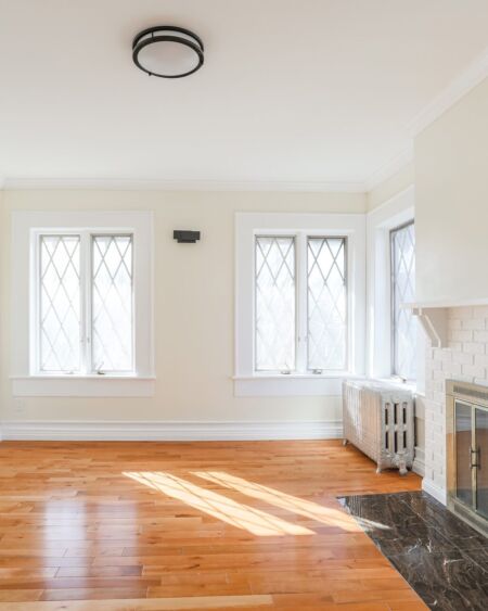 Empty living room with hardwood floors, a white brick fireplace, and leaded glass windows