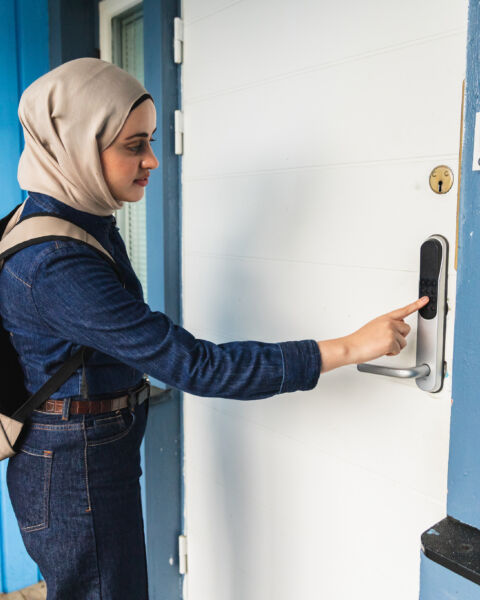 Woman in a hijab entering a code on a keypad lock at her door