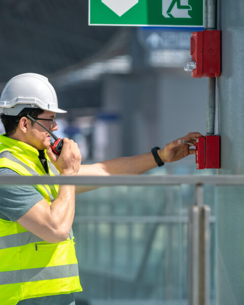 Worker in a hard hat and safety vest at an industrial site monitored for fire safety