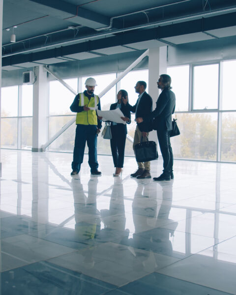 Business team are talking and looking around modern glass wall building standing inside discussing construction together. Real estate and commerce concept.