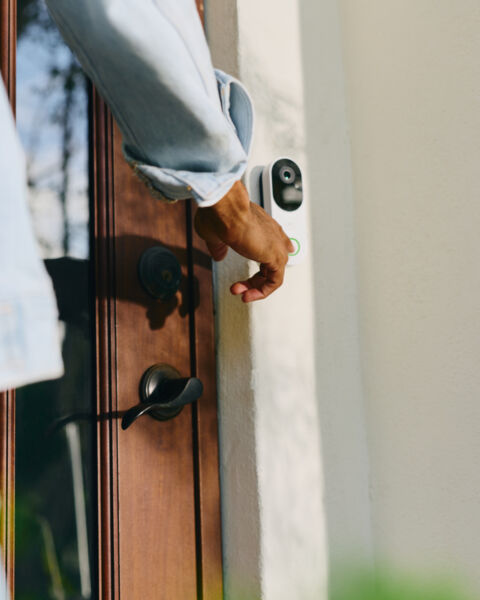 Hand reaching for the handle of a wooden front door with a video doorbell mounted beside it