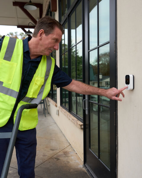 Worker in a safety vest using a video intercom to check in at a facility entrance
