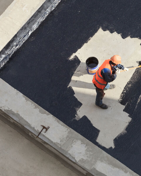 The worker in overalls applies an insulation coating on the concrete surface. View from above.
