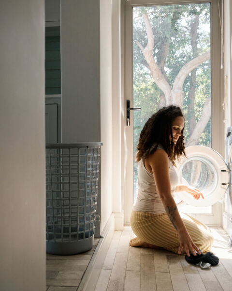 Woman crouching beside a washer and dryer in a laundry room