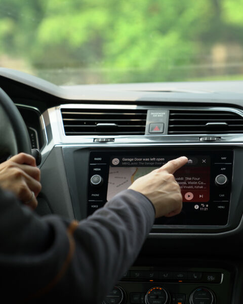 Hand reaching toward a car's touchscreen showing a garage door alert