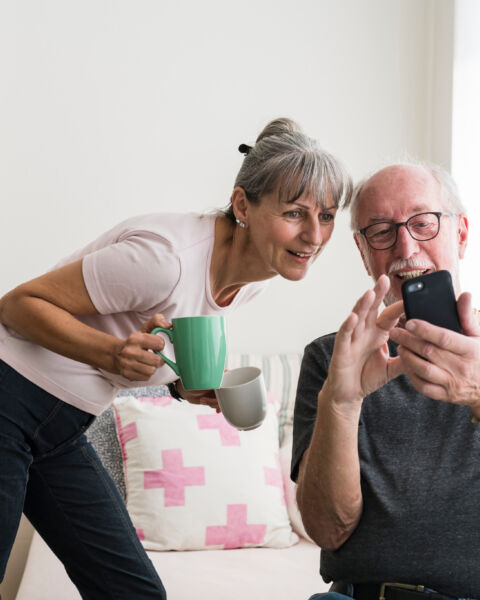 Older couple looking at a phone together, one holding a mug