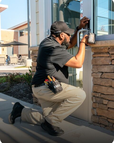 Installer kneeling to mount a security camera on the exterior wall of a building