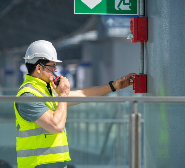 Worker in a hard hat and safety vest at an industrial site monitored for fire safety