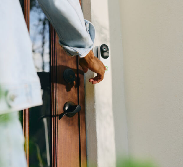 Hand reaching for the handle of a wooden front door with a video doorbell mounted beside it