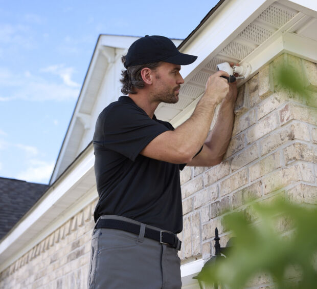 A technician mounting a security camera on the exterior of a house.