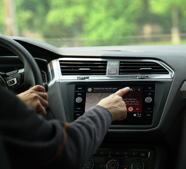 Hand reaching toward a car's touchscreen showing a garage door alert