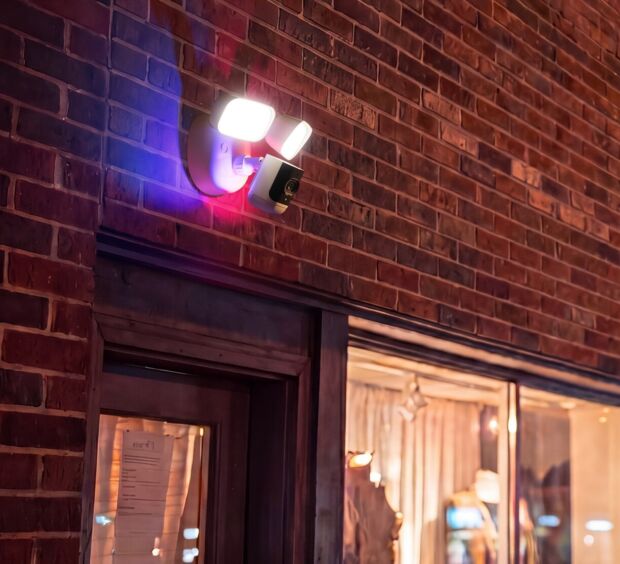Security camera with an activated floodlight and blue and red warning lights on a brick storefront