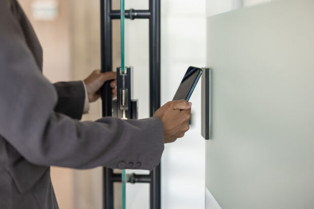Employee presenting a credential to a card reader beside a glass office door