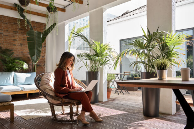 Employee working on a laptop in a plant-filled lounge area of a commercial building