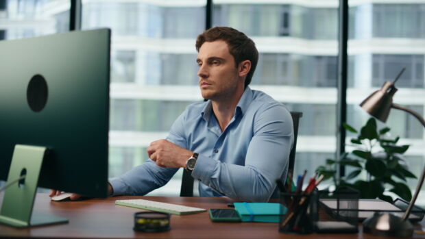 Sad office manager frustrated looking on computer monitor sitting at desk close up. Unhappy worker disappointed by corporate work results. Overworked man feeling exhausted tired on workplace.